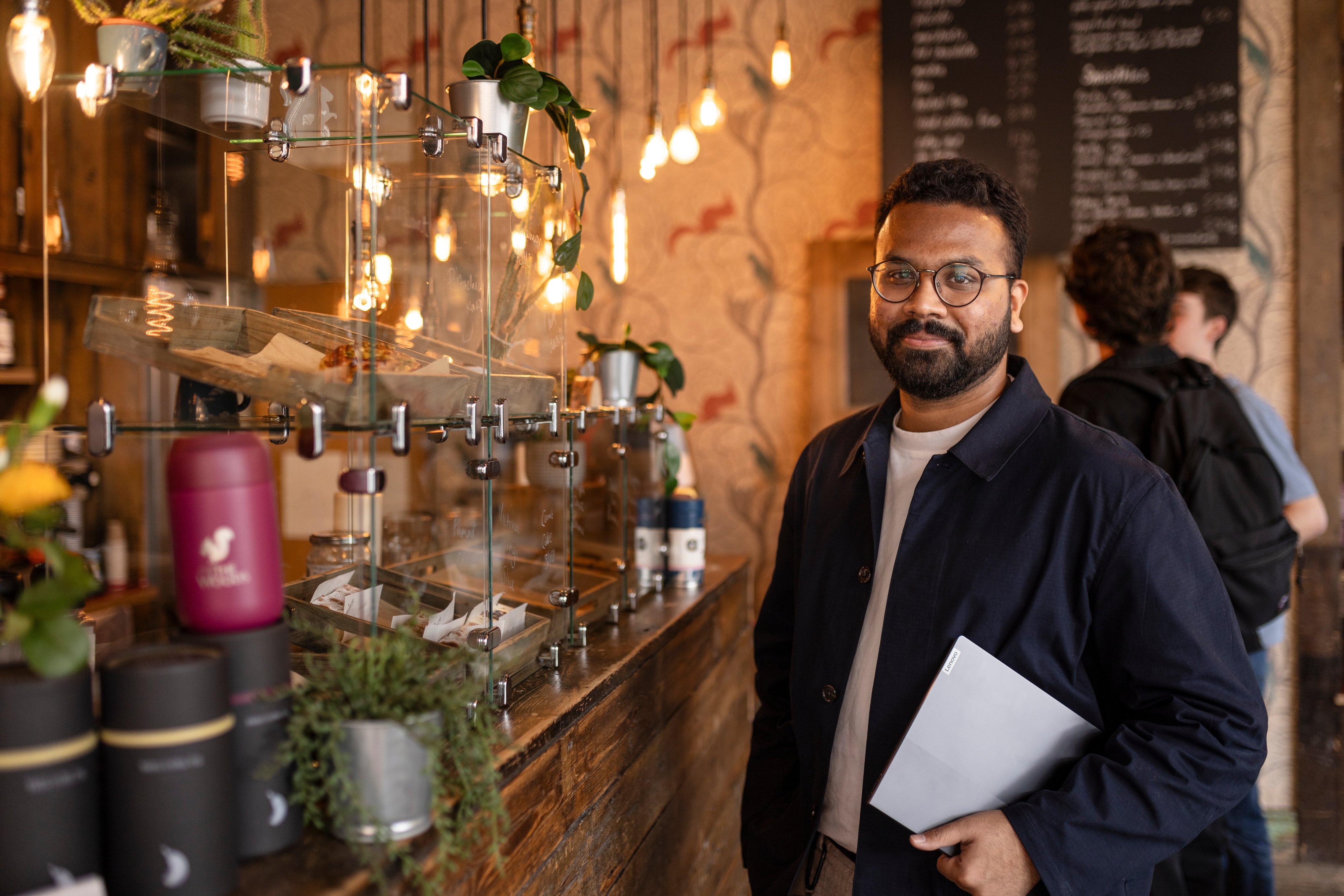 Student stood at cafe counter with laptop under his arm