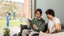 Two students sat on a sofa reviewing a tablet screen.