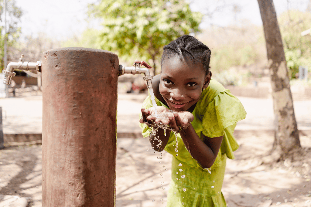 Little girl smiling at camera while drinking water